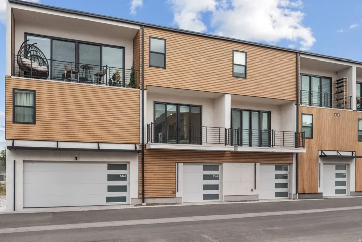 Modern multi-story exterior with wood-finish siding, private balconies with black railings, large glass sliding doors, and integrated garage doors with frosted window panels