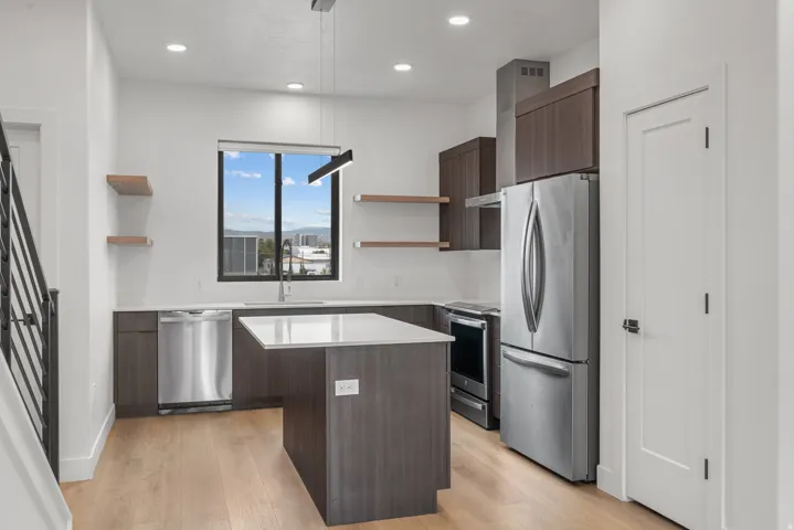 Kitchen featuring wood-finish flooring, dark wood-finish cabinetry, stainless steel appliances, a center island with a light-toned countertop, and recessed lighting