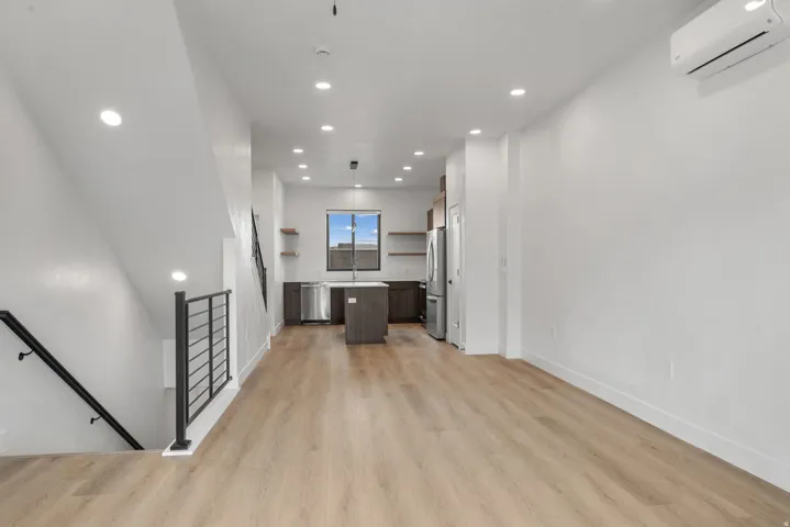 Open-concept living space with wood-finish flooring, recessed lighting, and a modern kitchen featuring stainless steel appliances, dark cabinetry, and a central island