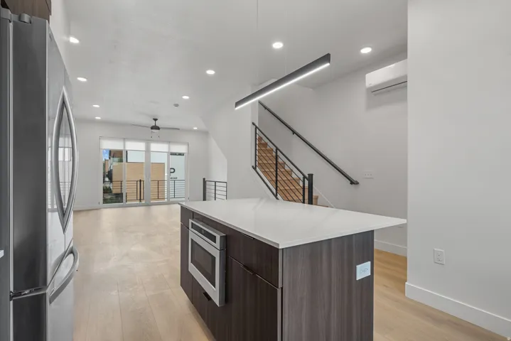 Open-concept interior featuring wood-finish flooring, a kitchen island with built-in microwave, and a contemporary linear light fixture