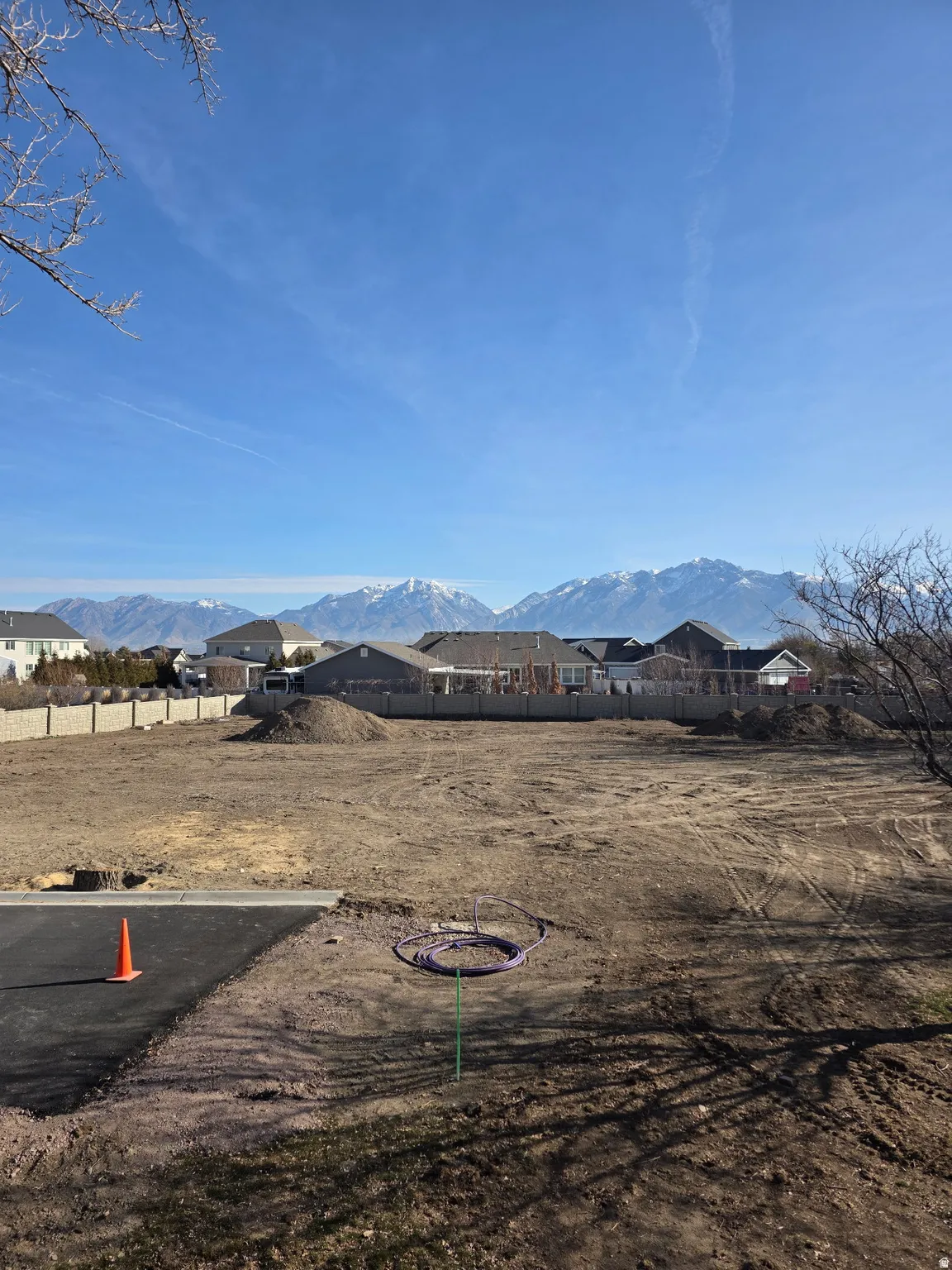Expansive lot featuring a graded surface, concrete block perimeter wall, and distant snow-capped mountains