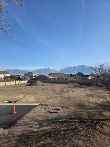 Expansive lot featuring a graded surface, concrete block perimeter wall, and distant snow-capped mountains