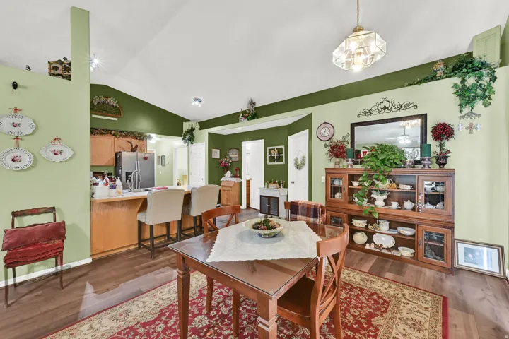 Open-concept living area featuring warm wood-finish flooring, soft green accent walls with crisp white trim, and abundant natural light from recessed ceiling fixtures