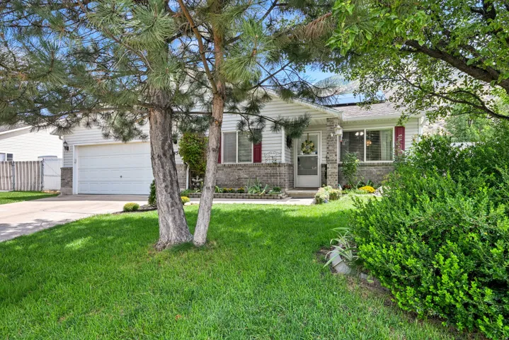 Landscaped front yard with mature trees, brick and siding exterior, front entry porch, attached garage, and paved driveway