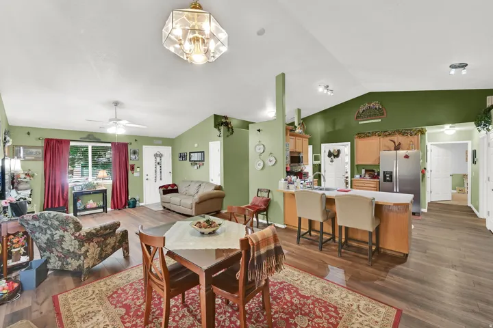 Open-concept living space featuring vaulted ceilings, wood-finish flooring, a kitchen island with seating, stainless steel refrigerator, and recessed lighting