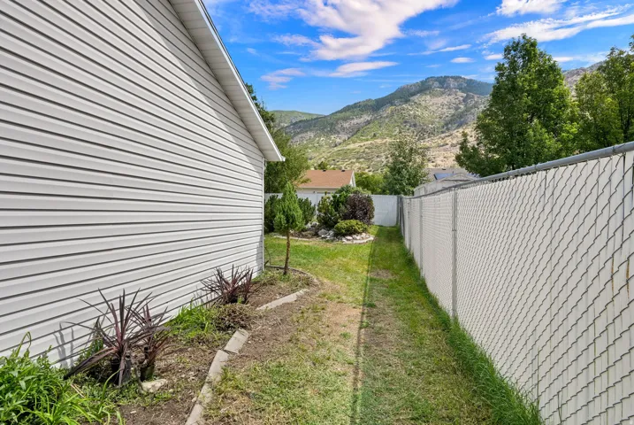 White vinyl siding, established landscaping, chain-link fencing, and a mountainous backdrop