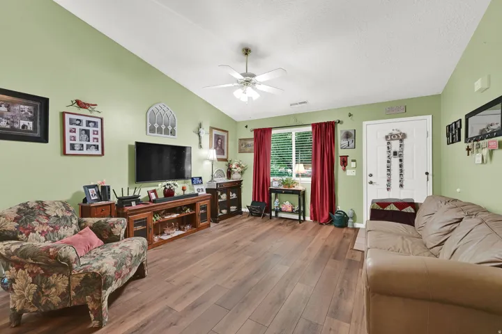 Vaulted ceiling with a ceiling fan, wood-finish flooring, and a white entrance door