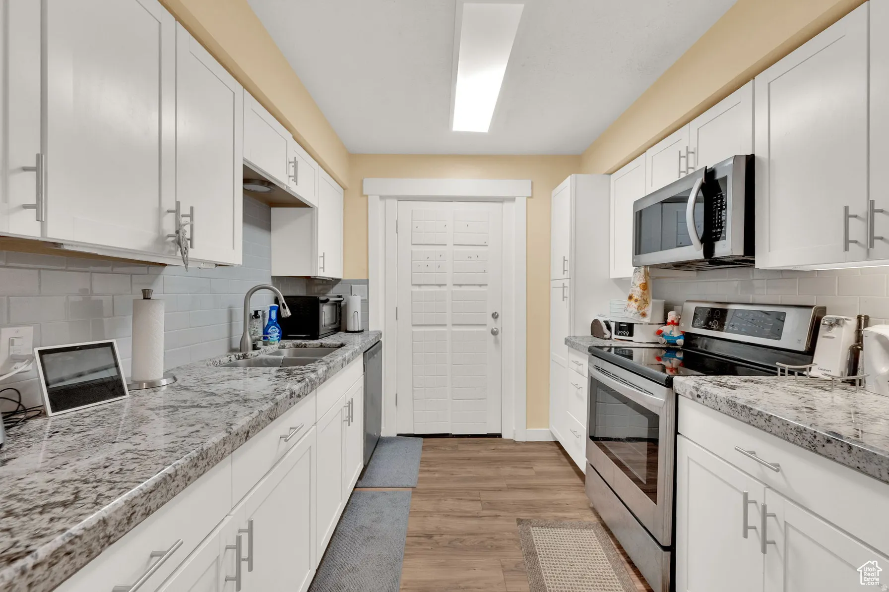 White cabinetry with brushed nickel hardware, stainless steel appliances, speckled countertops, subway tile backsplash, and wood-finish flooring