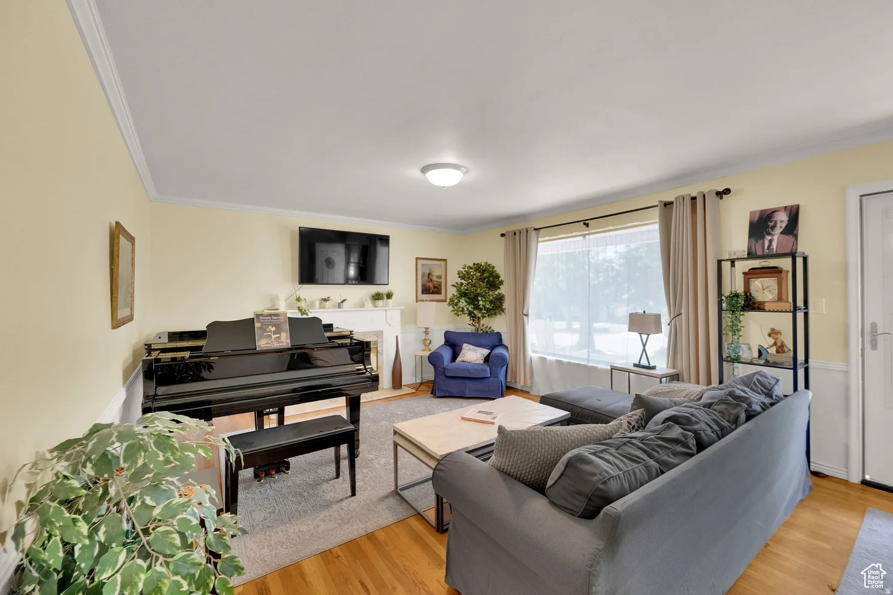 Living area featuring wood-finish flooring, crown molding, a fireplace with a white mantel, and a large window with curtain rods