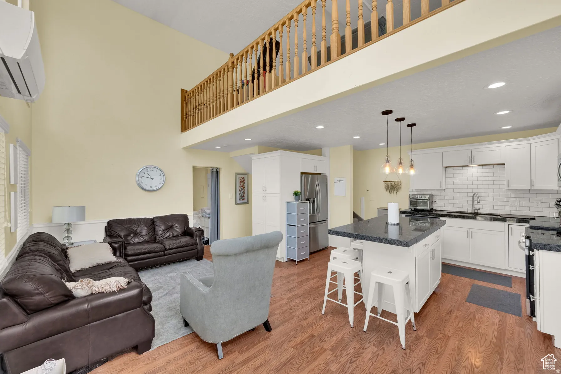 Vaulted ceiling living area with wood-finish flooring, a kitchen island with seating, pendant lighting, and white cabinetry