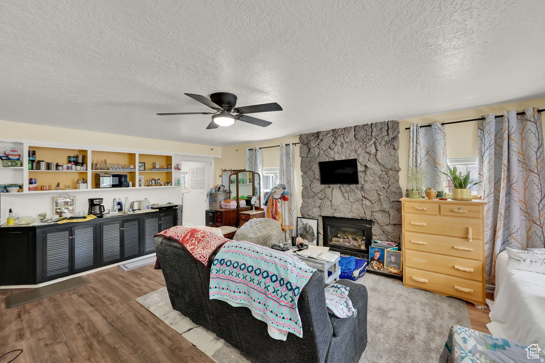 Wood-finish flooring, built-in shelving, stone-faced fireplace with hearth, and a ceiling fan