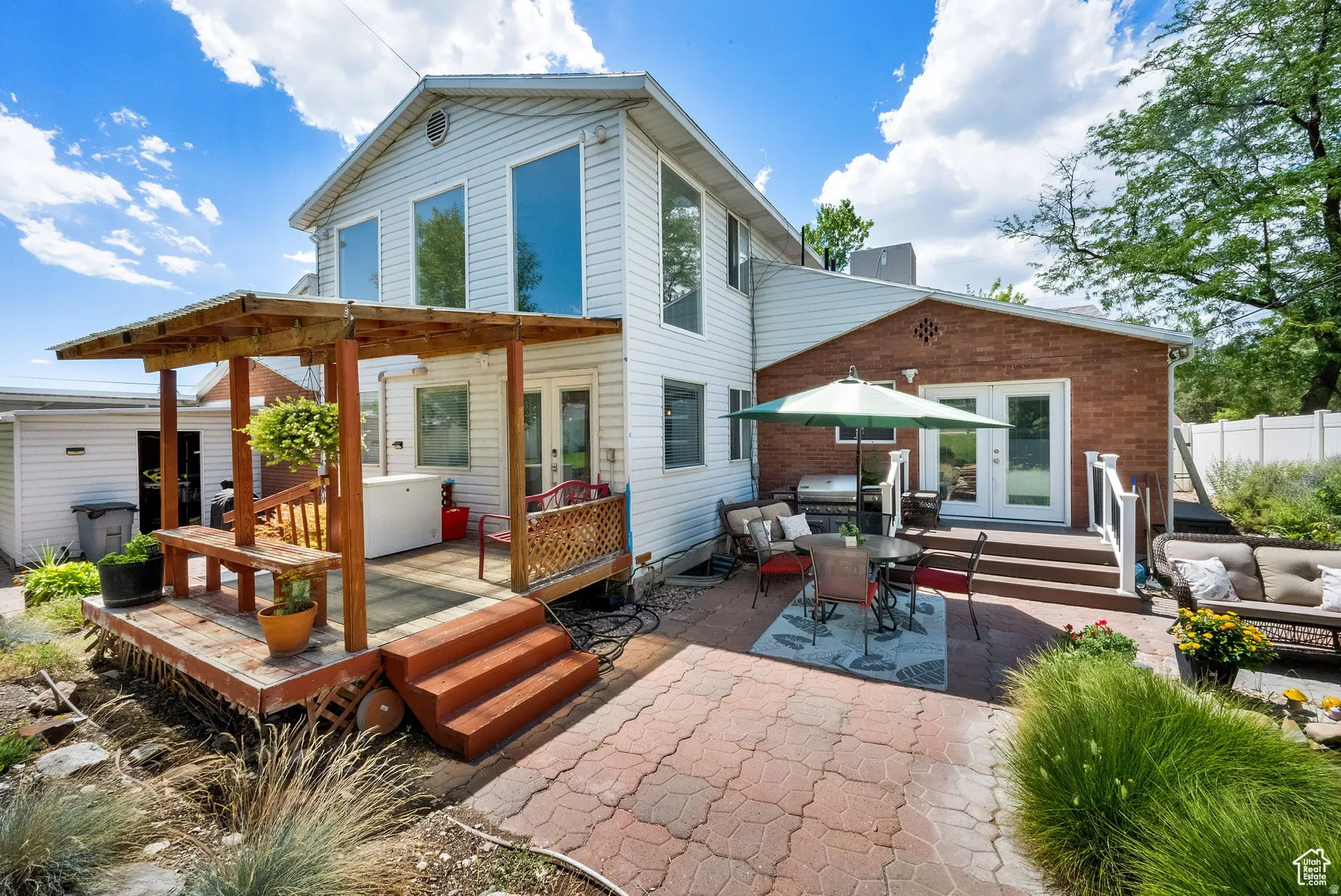Two-story exterior with white siding and brick accents, featuring a multi-level wood deck with pergola, a paved patio, and a separate storage shed