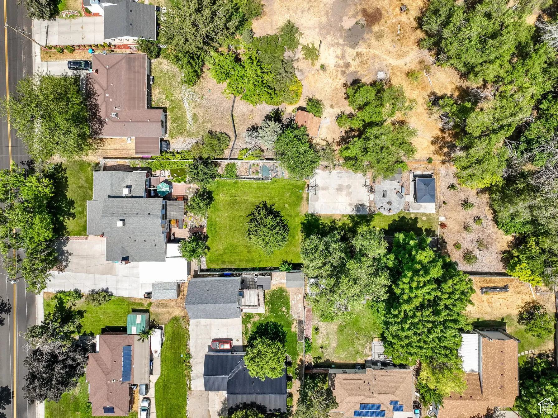 Spacious property featuring a large main residence, expansive green lawn, mature trees, paved patio area, and a private gazebo