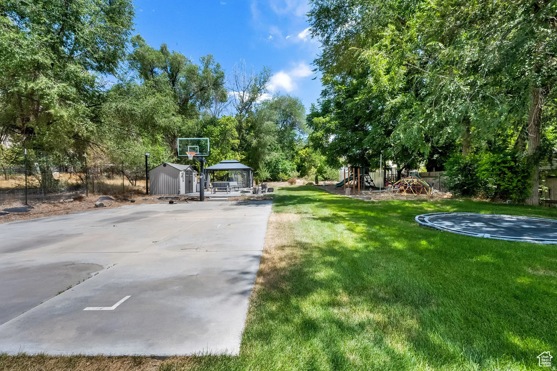 Expansive backyard featuring a concrete sport court, covered gazebo, storage shed, and mature trees