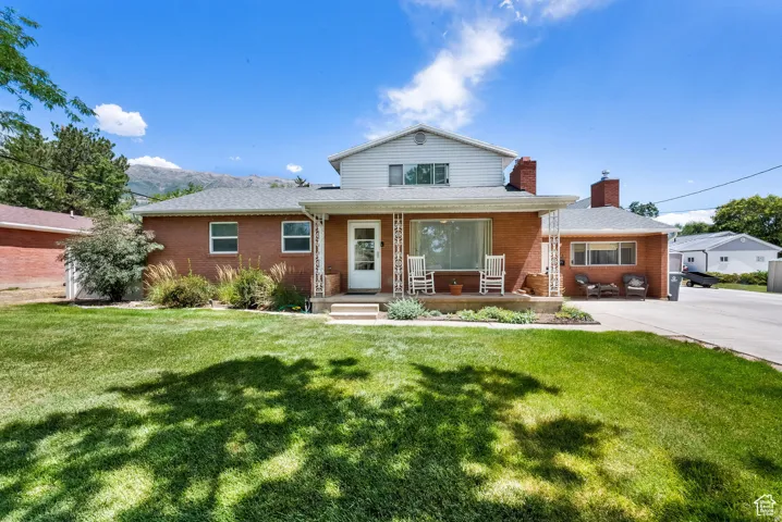 Brick exterior with white siding accents, covered front porch, established landscaping, and a paved driveway