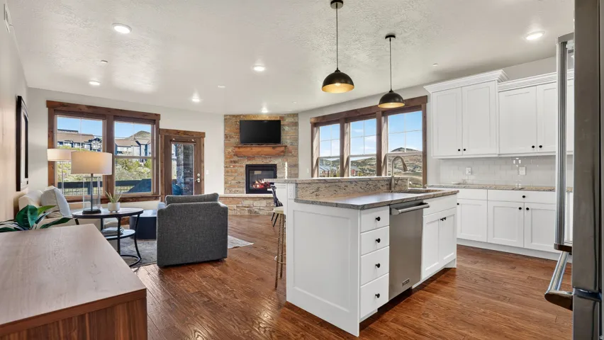 Open-concept living area with wood-finish flooring, a stone-surround fireplace, and large windows