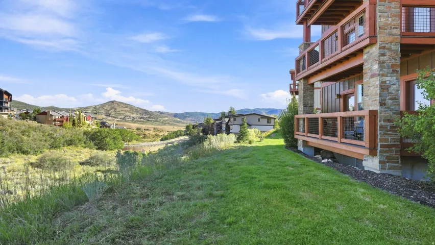 Stone and wood-clad exterior with multiple balconies, a manicured lawn, and expansive natural scenery