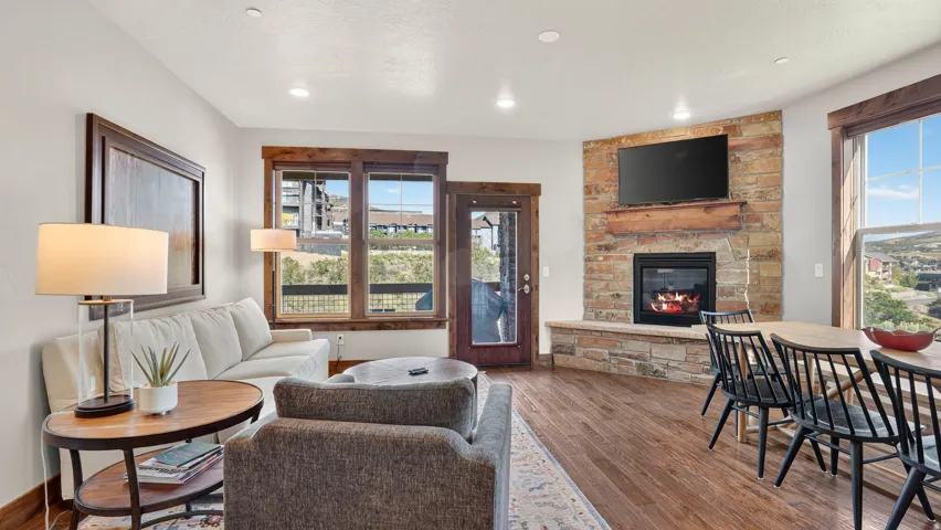 Spacious living area featuring wood-finish flooring, a stacked stone fireplace with a wood mantle, and recessed lighting