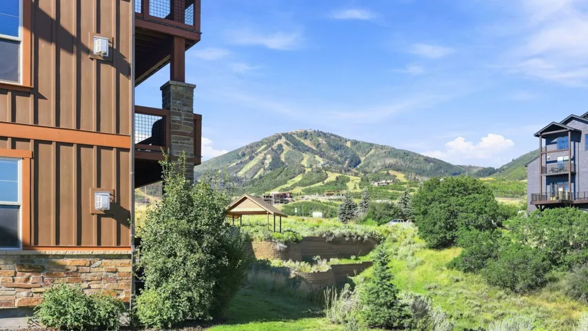 Mountain backdrop with visible ski runs, board and batten siding, stone accents, and a multi-level deck with metal railing
