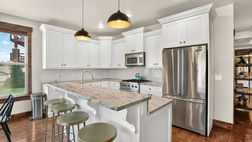 Kitchen with white cabinetry, stainless steel appliances, granite countertops, and wood-finish flooring