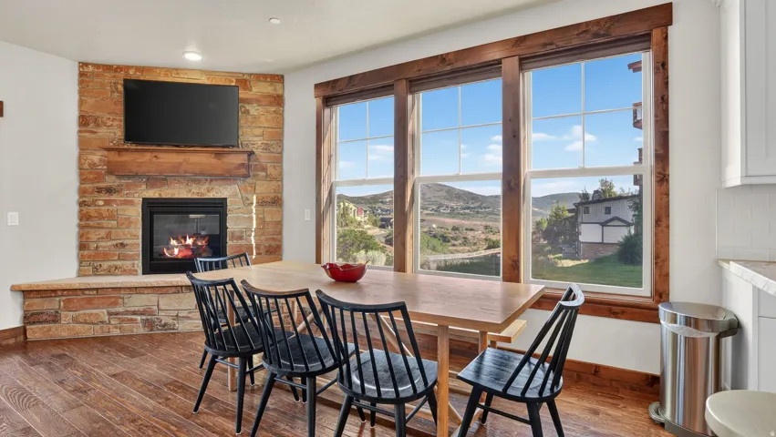 Built-in stone fireplace with a wood mantle, wood-finish flooring, and a wall of windows featuring wood trim