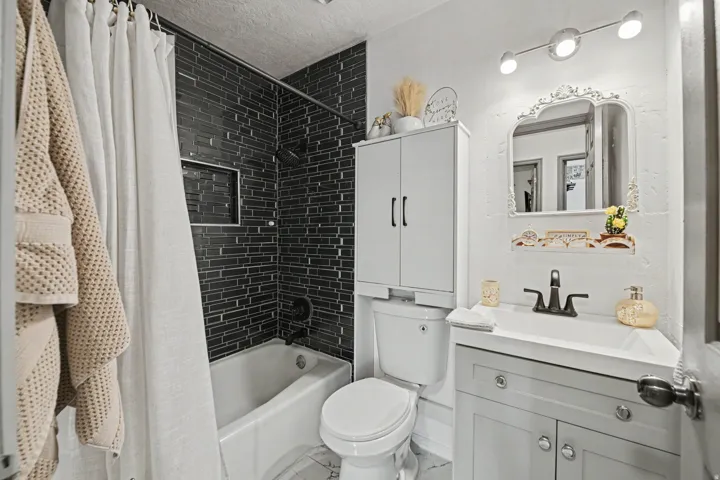 Modern bathroom featuring a subway tile shower surround with integrated tub, white vanity cabinetry with brushed nickel hardware, vessel sink with matte black faucet, mirrored medicine cabinet with integrated lighting, and tile flooring throughout