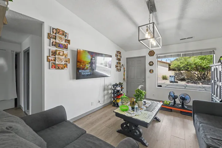 Spacious living area featuring wood-finish flooring, a contemporary ceiling light fixture, a large window, and a paneled entry door