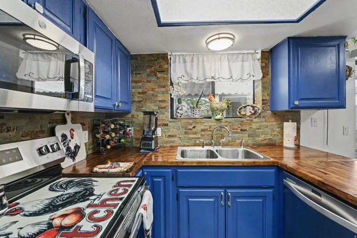 Vibrant blue cabinetry, wood-finish countertops, stainless steel appliances, stacked stone backsplash, and a double basin stainless steel sink