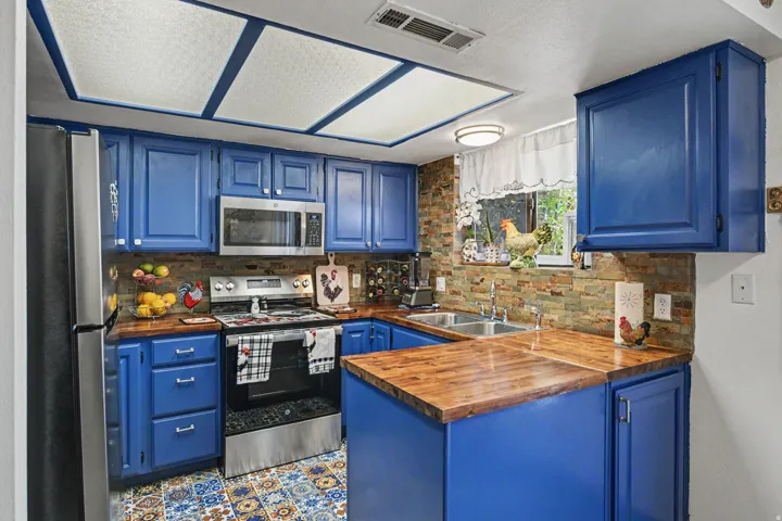Kitchen featuring blue cabinetry, wood-finish countertops, stainless steel appliances, a stacked stone backsplash, and decorative floor tiling