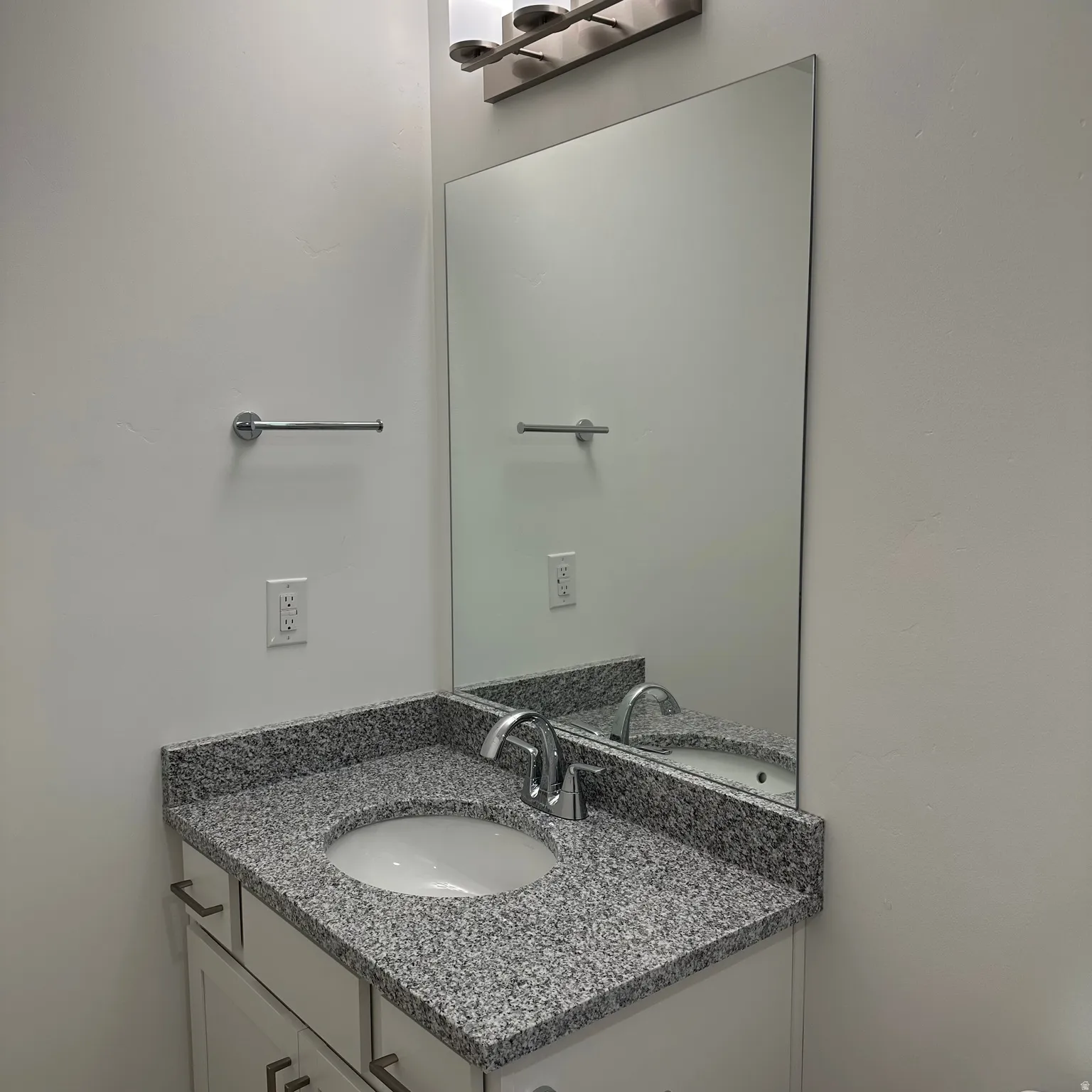 White vanity with silver-tone pulls, a granite-finish countertop, and an undermount sink