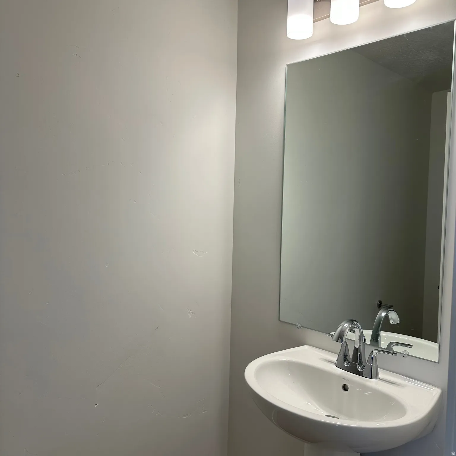 Pedestal sink with chrome faucet, large wall mirror, and modern three-light vanity fixture