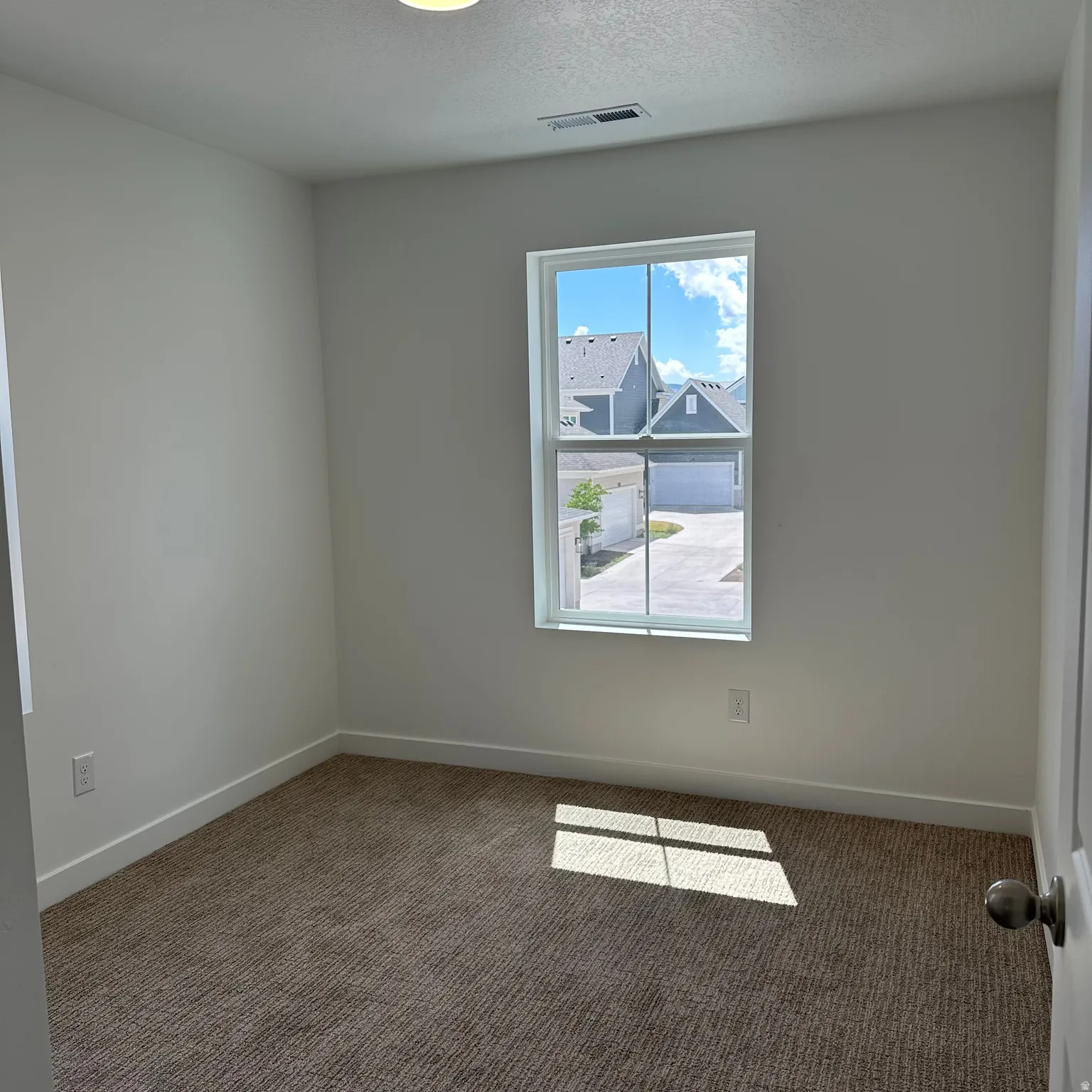Textured carpet flooring, white walls, white trim, single window, and flush-mount ceiling light