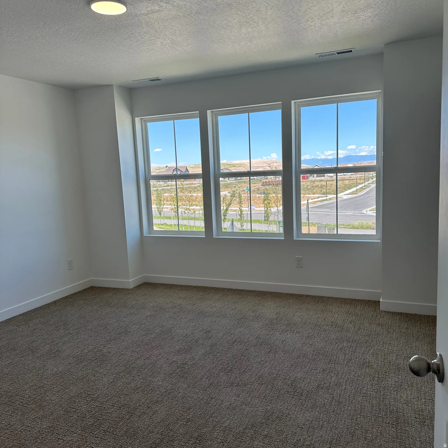 Three large windows, neutral-toned carpeting, and a flush-mount ceiling light fixture