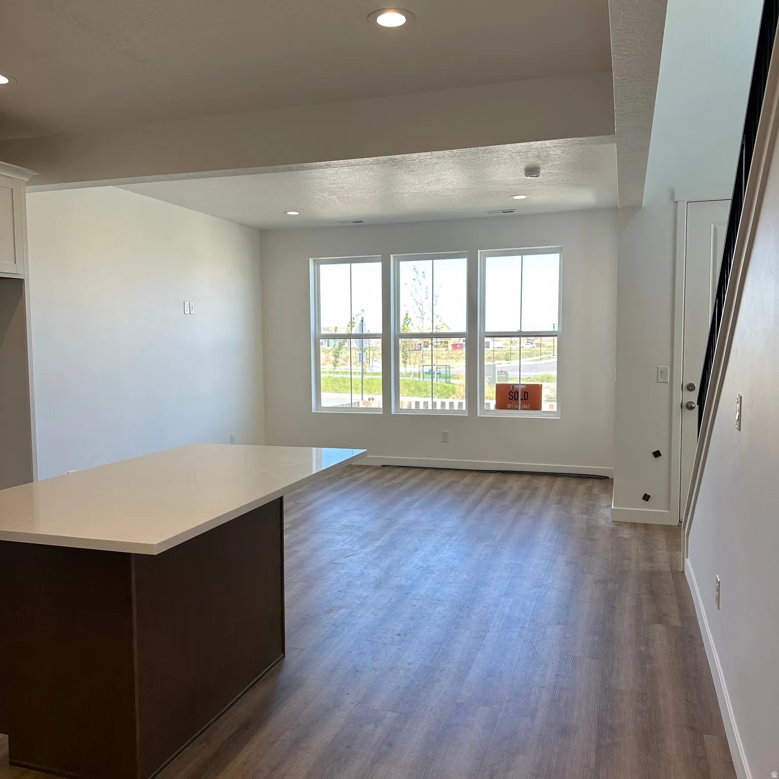 Spacious open-concept area featuring wood-finish flooring, a kitchen island with a light-toned countertop, and recessed lighting