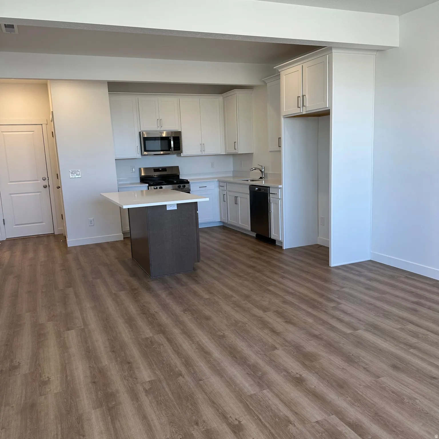 Modern kitchen featuring white cabinetry, stainless steel appliances, a center island with a light-toned countertop, and wood-finish flooring
