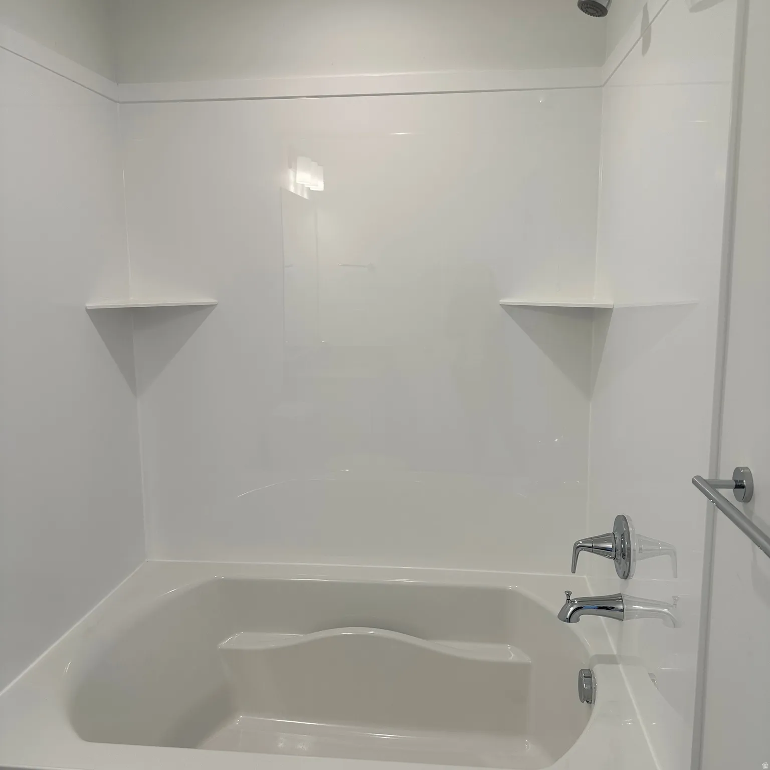 White fiberglass tub and shower combination with two integrated corner shelves and a chrome shower fixture