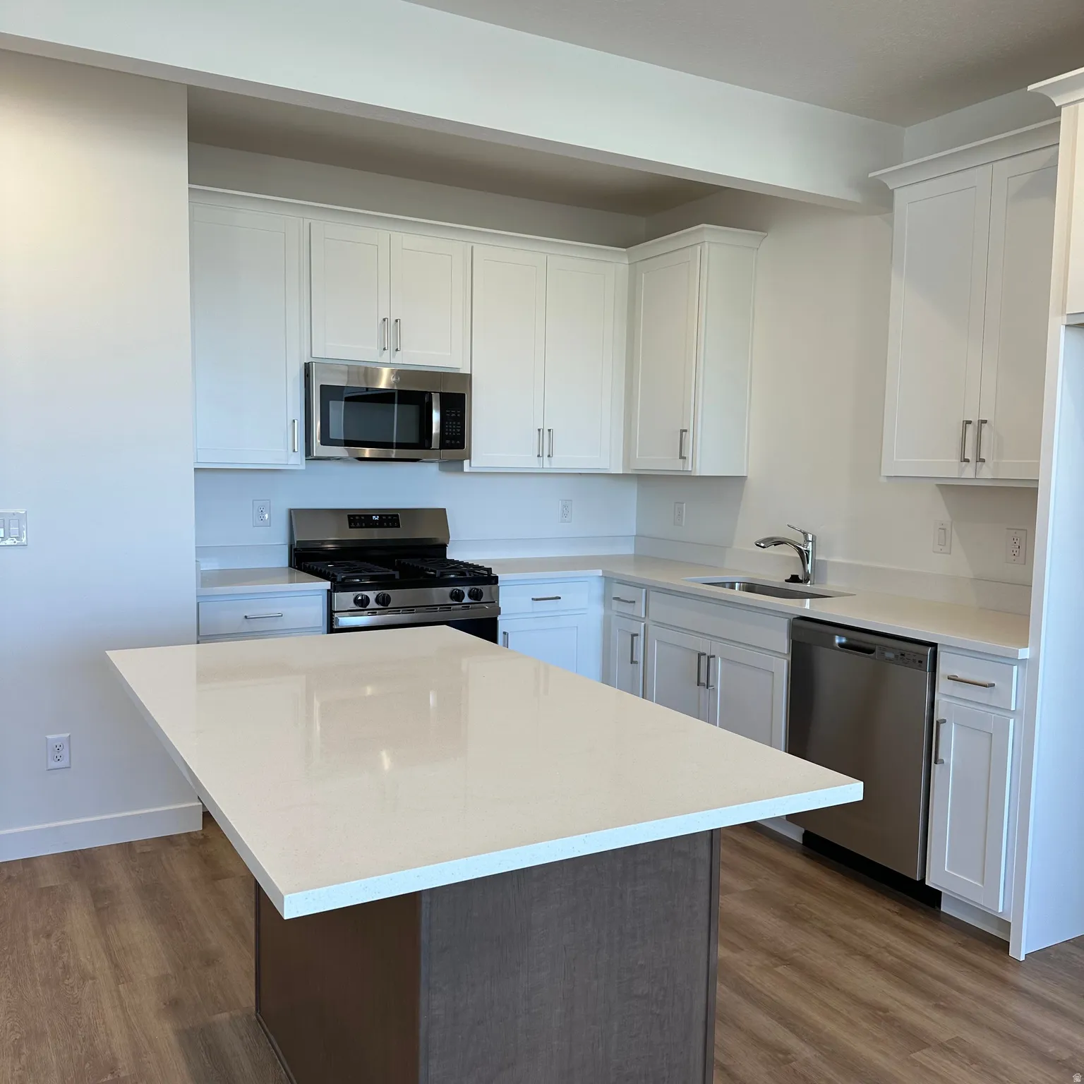 Kitchen featuring white cabinetry, stainless steel appliances, wood-finish flooring, a kitchen island, and light-colored countertops