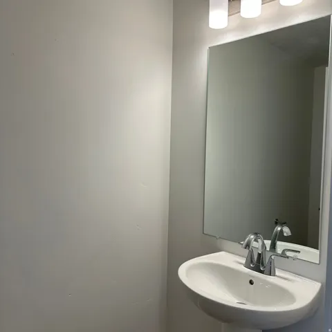 Pedestal sink with chrome faucet, large wall mirror, and modern three-light vanity fixture
