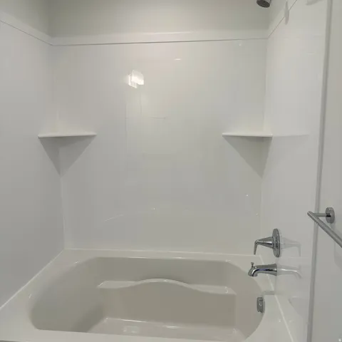 White fiberglass tub and shower combination with two integrated corner shelves and a chrome shower fixture