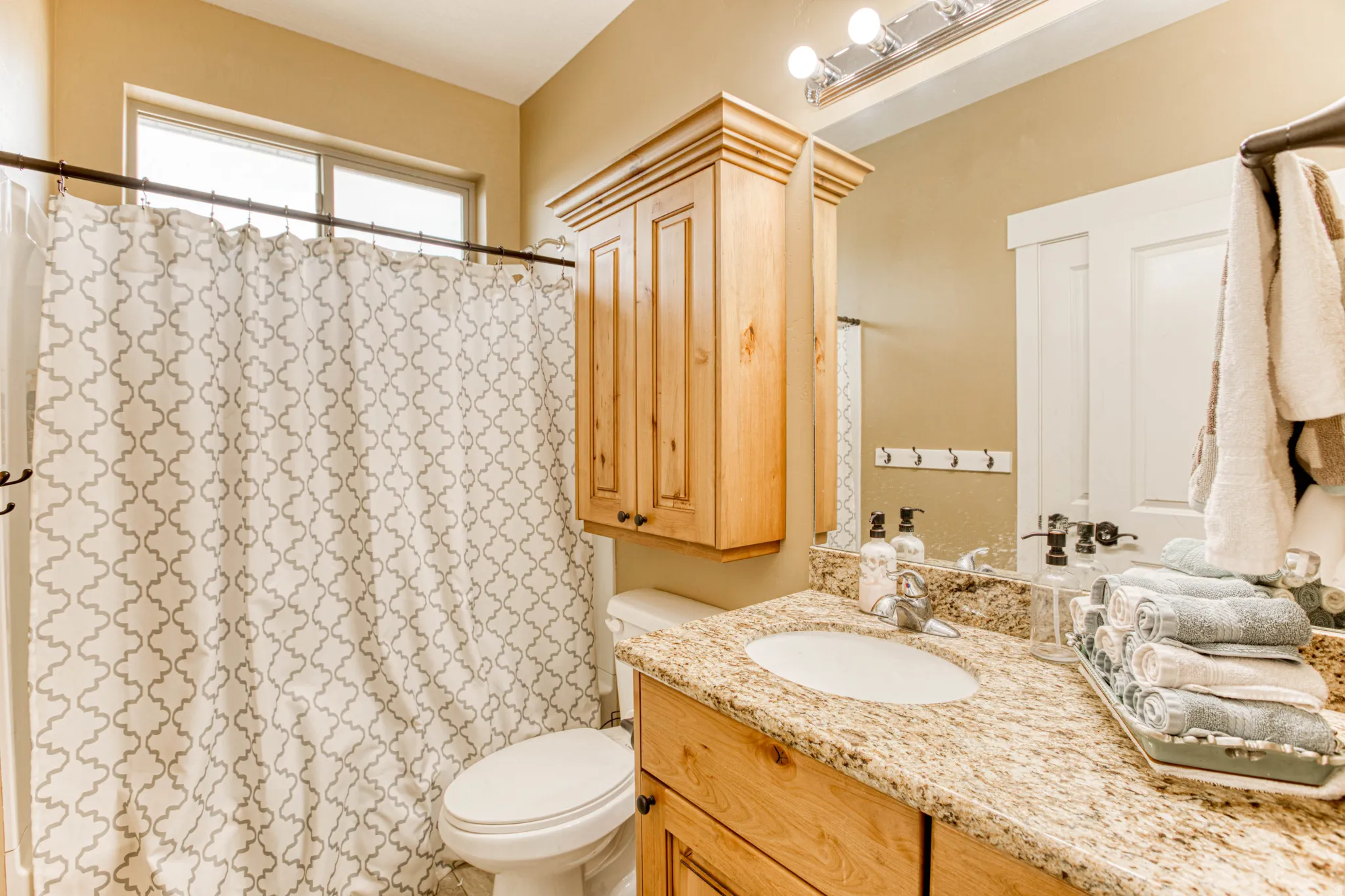 Single vanity with a granite countertop, undermount sink, and wood-finish cabinetry