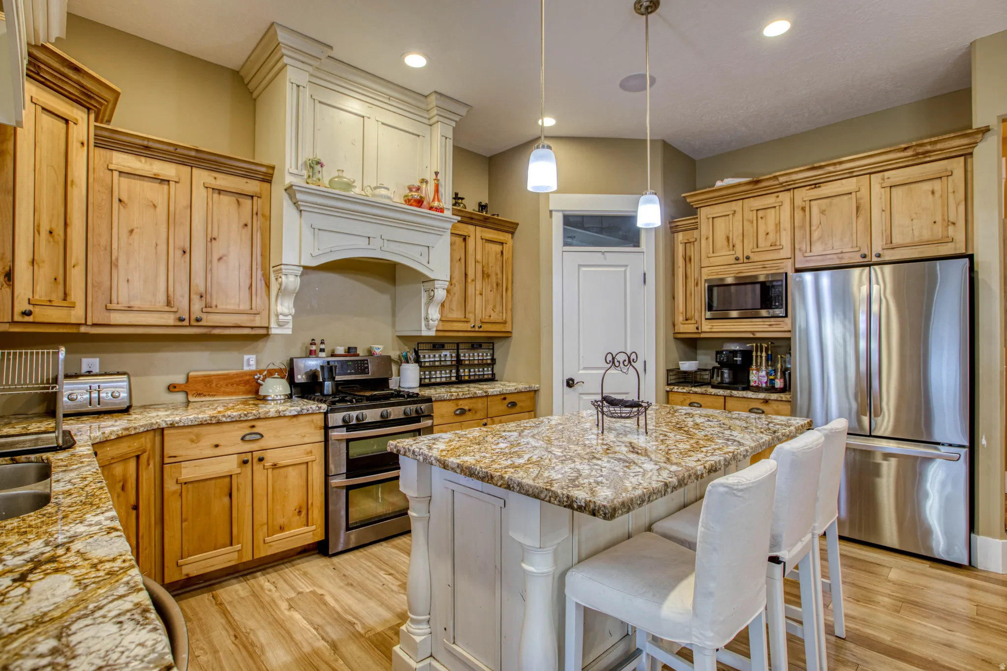 Kitchen featuring a large island, wood-finish flooring, stainless steel appliances, custom cabinetry, and pendant lighting