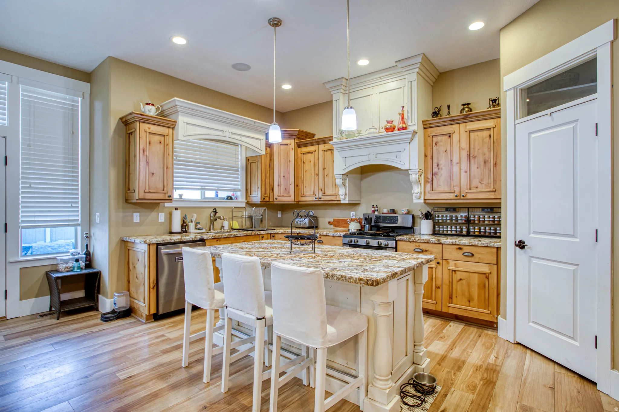 Kitchen featuring wood-finish flooring, natural wood cabinetry, stainless steel appliances, a multi-tonal countertop, and a center island with seating