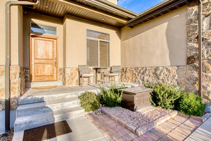 Stucco exterior with stone veneer accents, wood-paneled entry door with transom window, concrete steps, and paver pathway