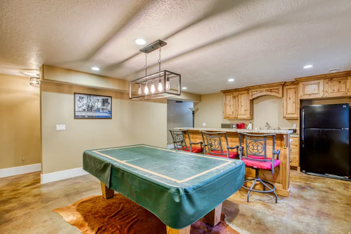 Recreational area featuring a wet bar with wood cabinetry, granite-finish countertops, and a full-size refrigerator