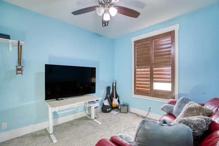 Carpeted interior space featuring a ceiling fan with integrated lighting, wood-finish plantation shutters, and white trim