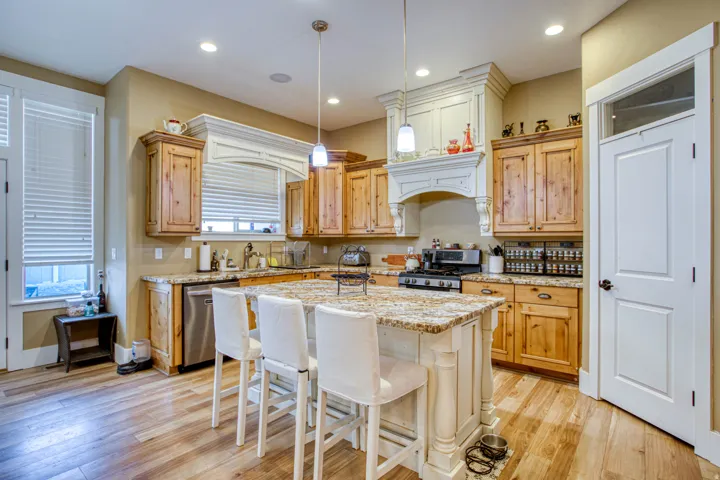 Kitchen featuring wood-finish flooring, natural wood cabinetry, stainless steel appliances, a multi-tonal countertop, and a center island with seating