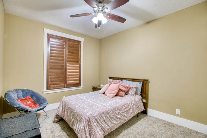 Textured carpet flooring, window with wood-finish shutters, ceiling fan with light fixture, and white trim molding