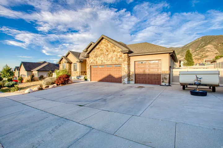 Stone and stucco exterior with multiple garage doors, a concrete driveway, and established landscaping