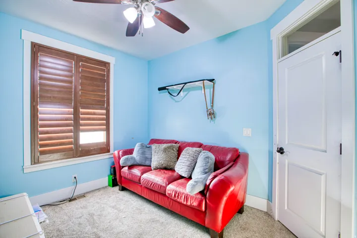 Ceiling fan with light fixture, window with wood shutters, white trim, paneled door, and carpeted flooring