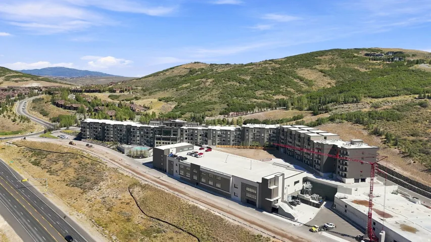 Modern building complex with multiple balconies, adjacent to a highway and surrounded by natural, undeveloped hillsides